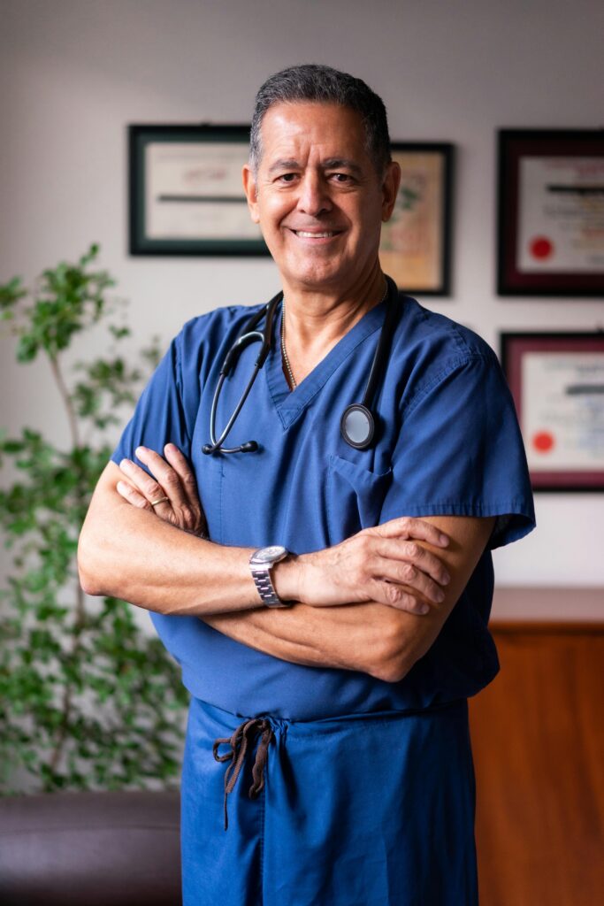 Smiling male healthcare professional in blue scrubs with arms crossed indoors.